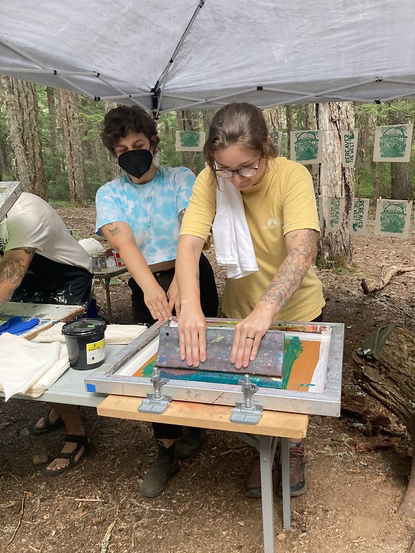 daniela and a volunteer screen printing with green ink in a tent at a campout