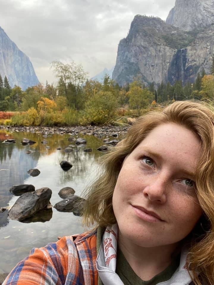 This image shows Haley looking up towards the sky in a beautiful outdoor setting. She has strawberry blonde hair and is wearing a plaid red and blue shirt.