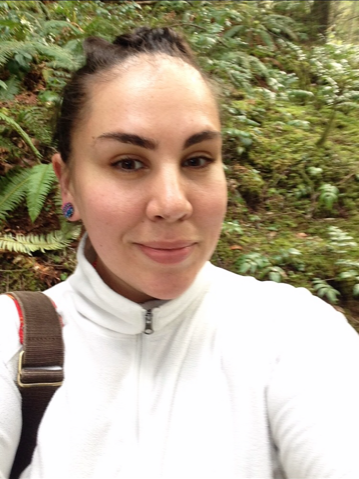 Headshot of Jessie wearing a white zip up in front of sword ferns