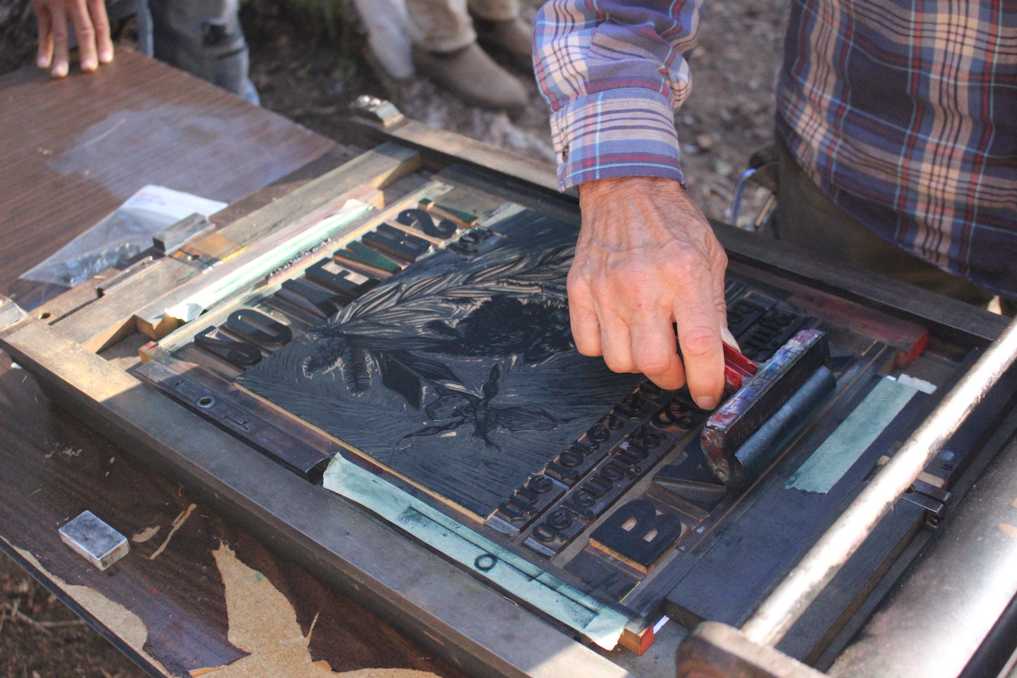 A person's hand is holding an inking roller and is running it across a plate on an old fashioned letterpress.
