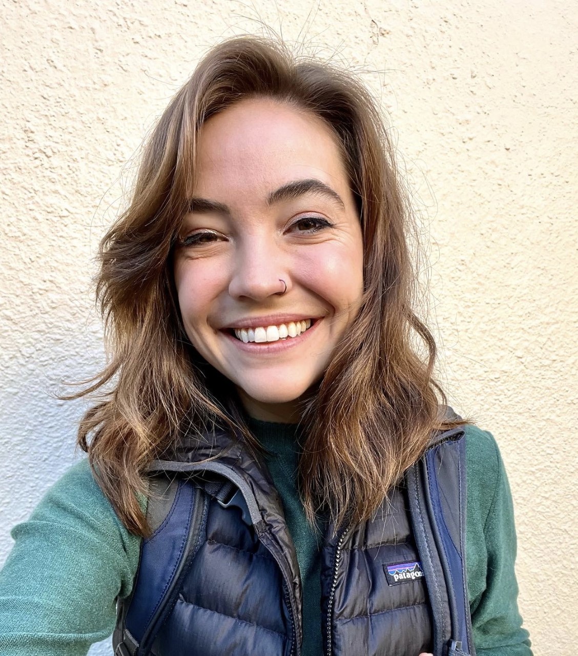 Color photo of Suze. She has shoulder-length medium brown hair and has a big smile on her face. She is wearing a green sweater and puffy black vest.